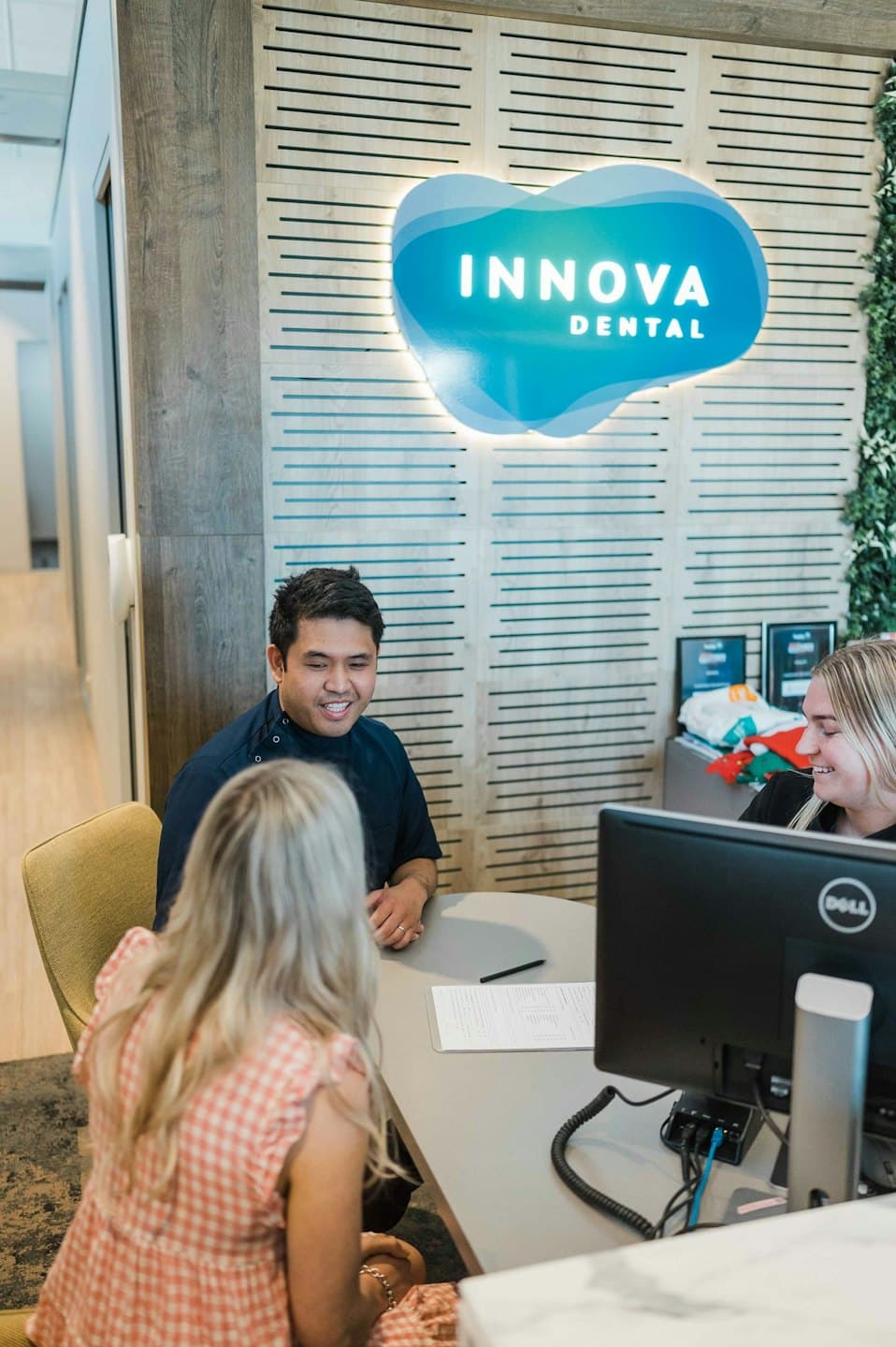 Staff and a patient talk at a dental office reception desk.