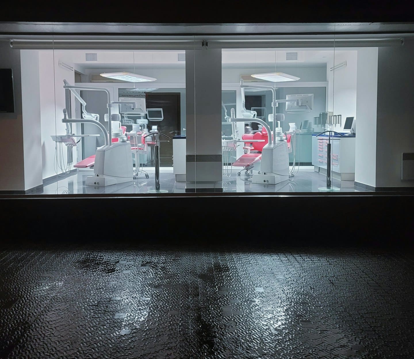 Modern dental clinic treatment rooms with red chairs at night.